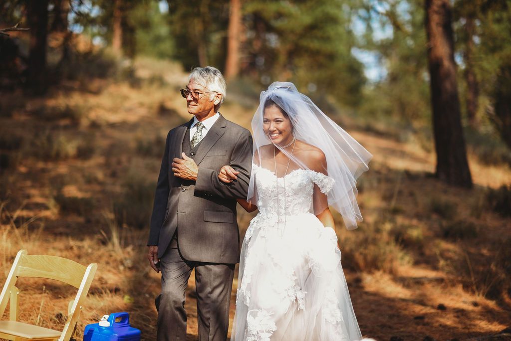 A joyful moment captured during an outdoor forest wedding ceremony with pine trees in the background.