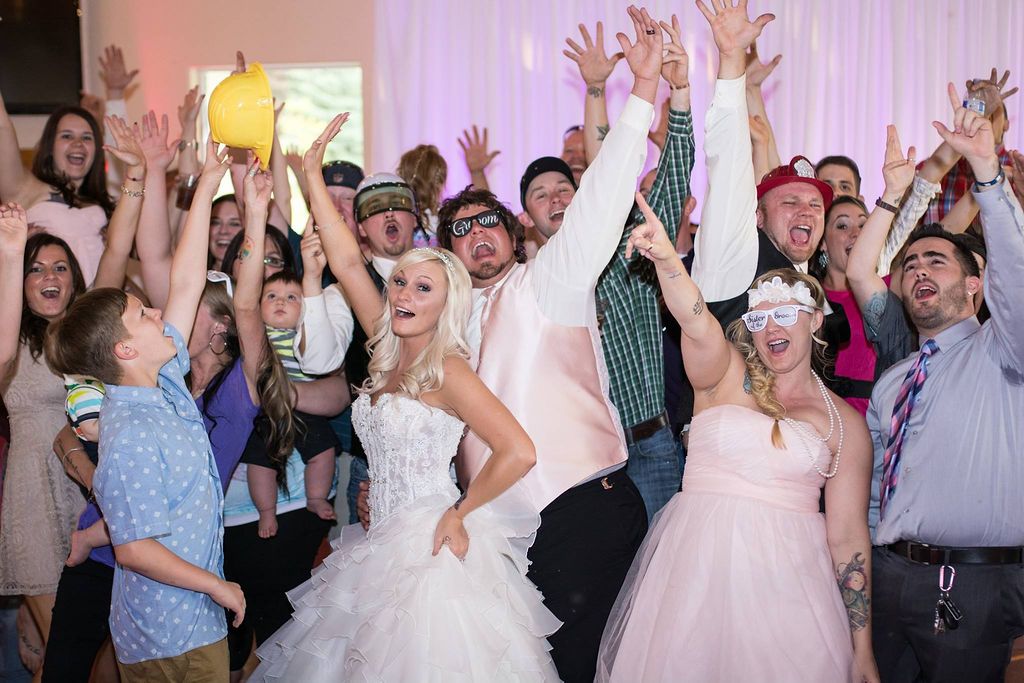 Energetic wedding reception crowd with partygoers jumping and raising their hands in celebration.
