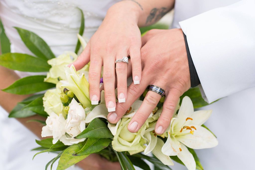 Close up of wedding rings and hands resting on white and green lily bouquet showing newlywed couple's jewelry.