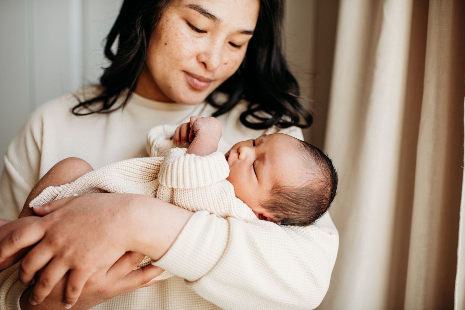 Peaceful newborn baby wrapped in cream colored clothing being cradled with gentle care.
