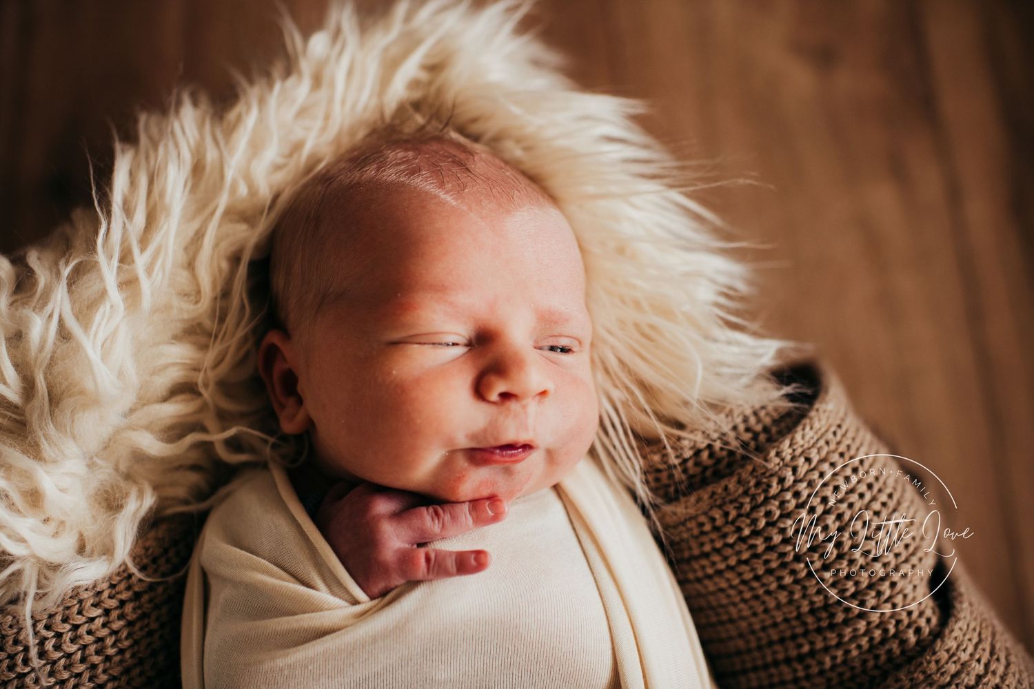 A newborn baby sleeps peacefully on a fluffy cream fur blanket.