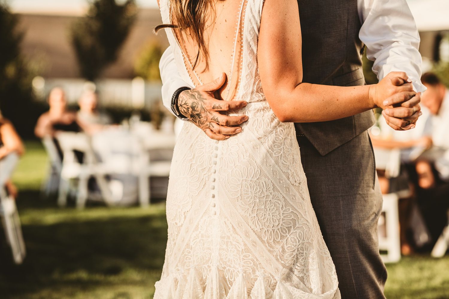 A couple shares a romantic dance outdoors at a wedding reception with white chairs visible in the background.