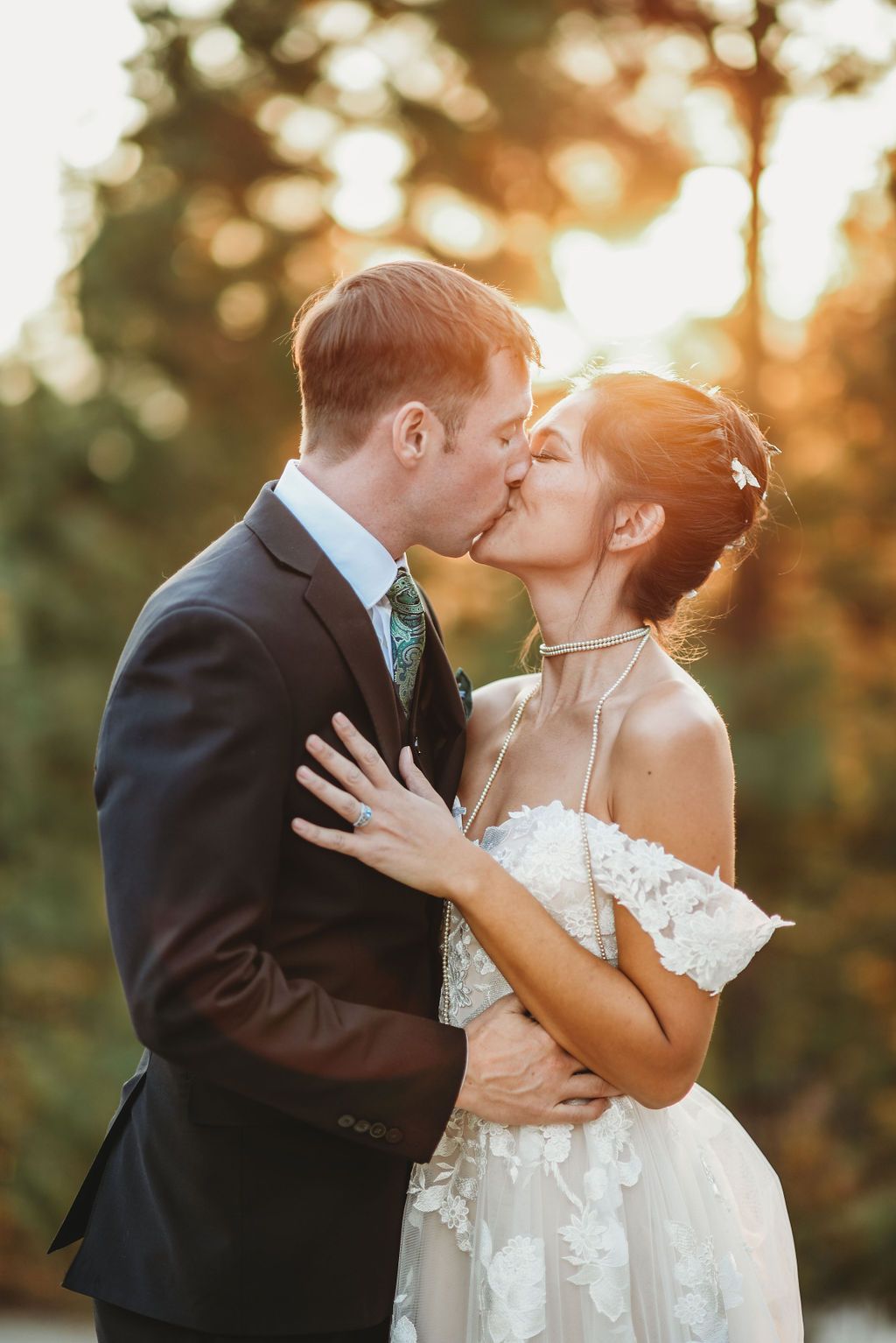 A romantic wedding couple shares a kiss at sunset with golden bokeh lighting in the background.