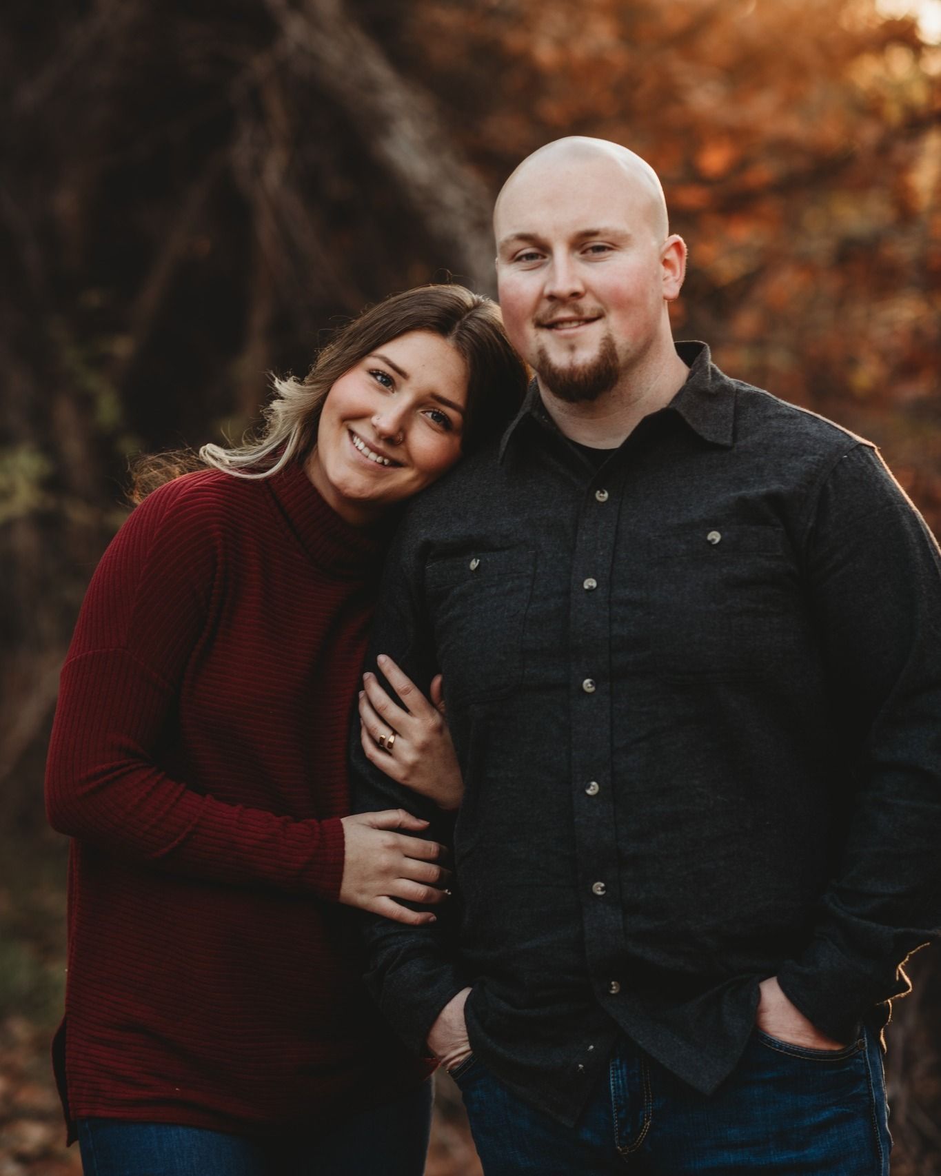 A couple in casual autumn attire shares a romantic moment against fall foliage.