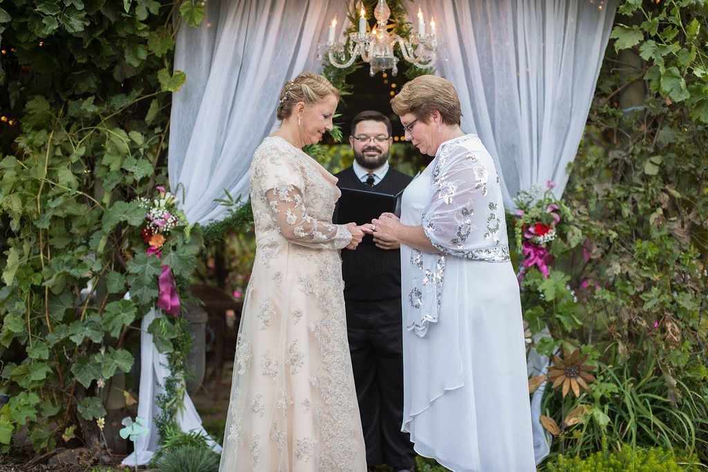 Wedding ceremony under an elegant draped arch with floral decorations and greenery in an outdoor garden setting.