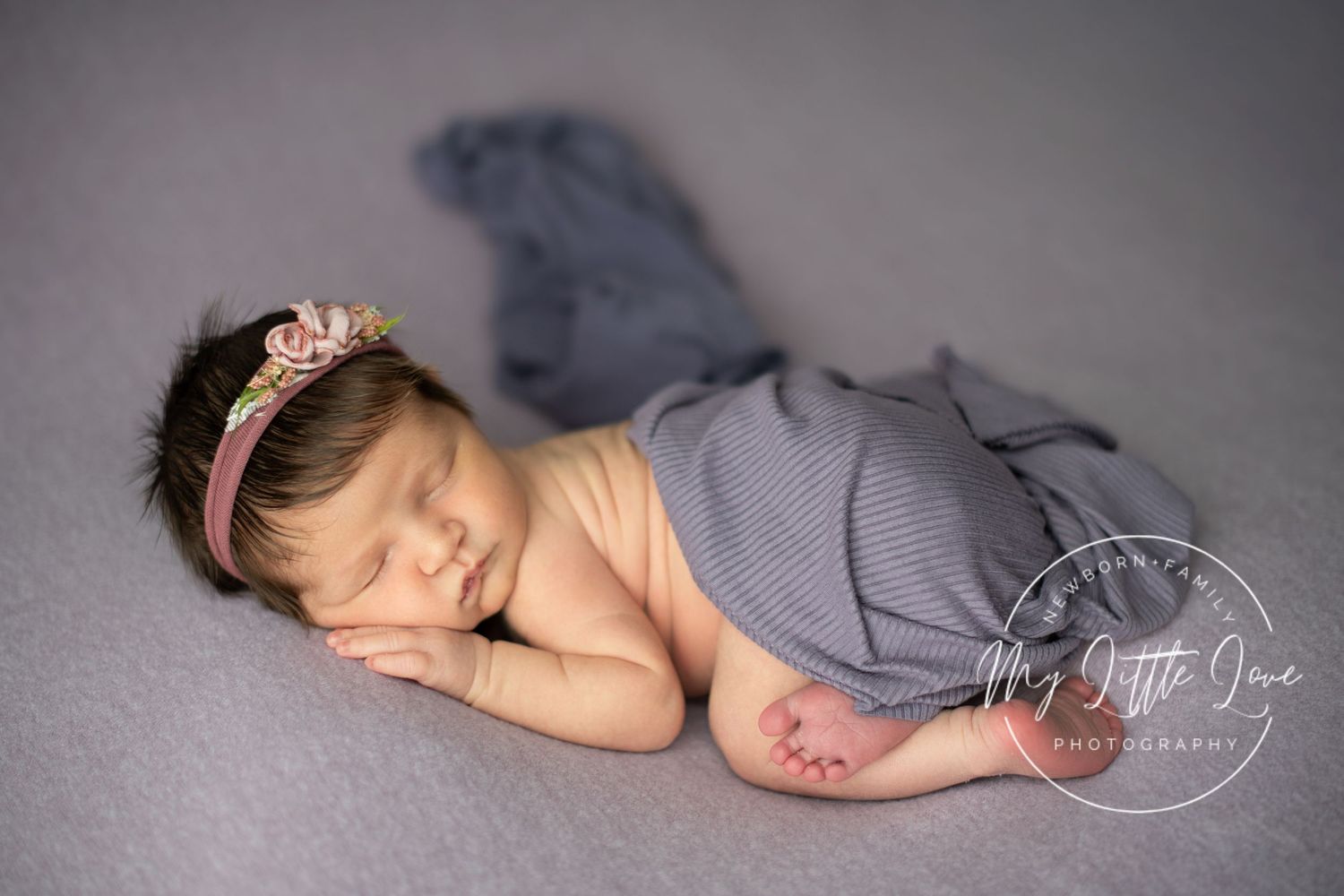 A sleeping newborn baby in gray wrap lies peacefully on a soft blanket during professional photography session.