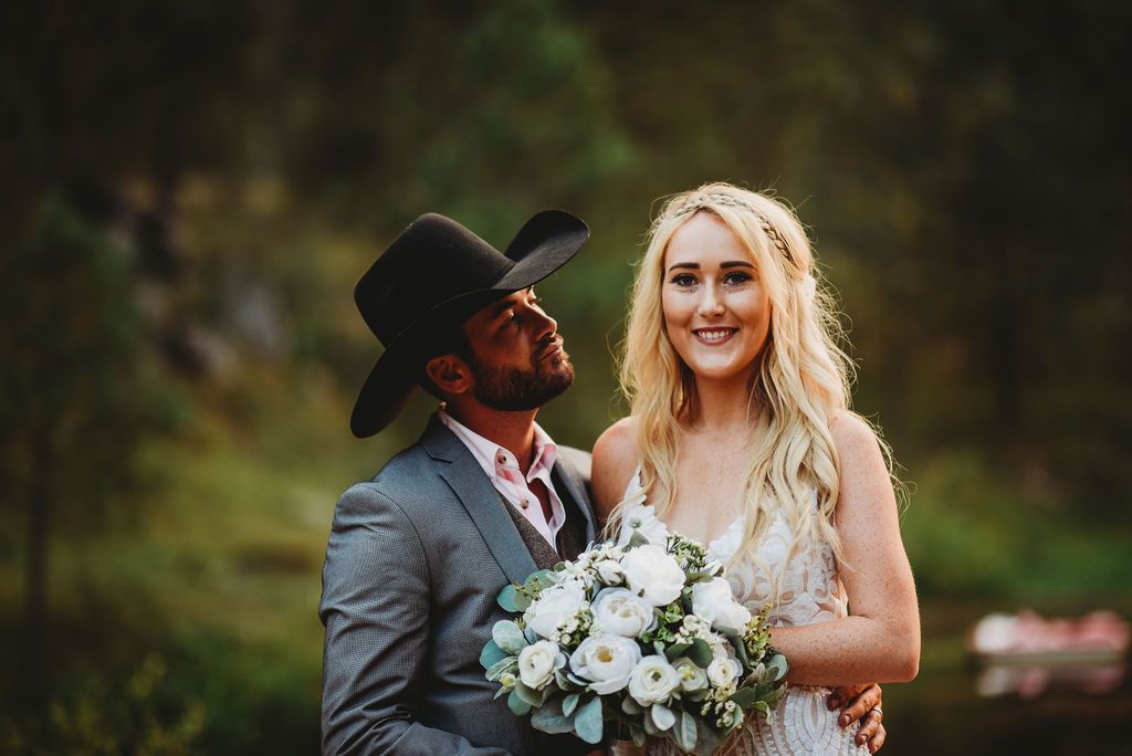 A wedding couple shares a candid moment outdoors as they hold a white and blue floral bouquet.