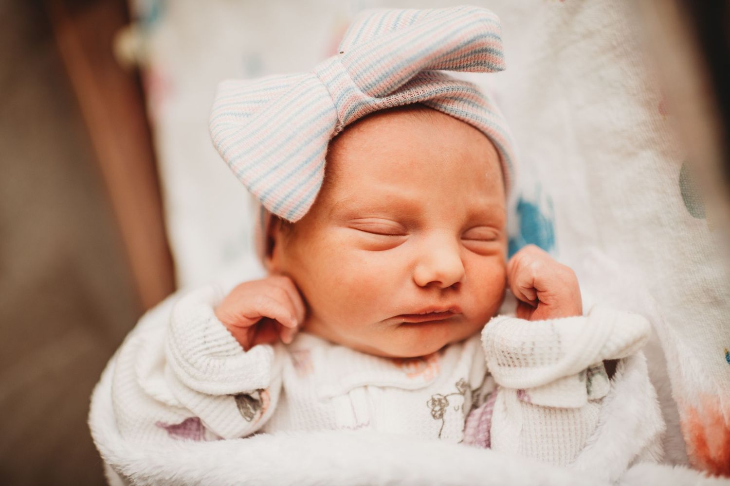 Sleeping newborn wearing white knit outfit with large bow headband.