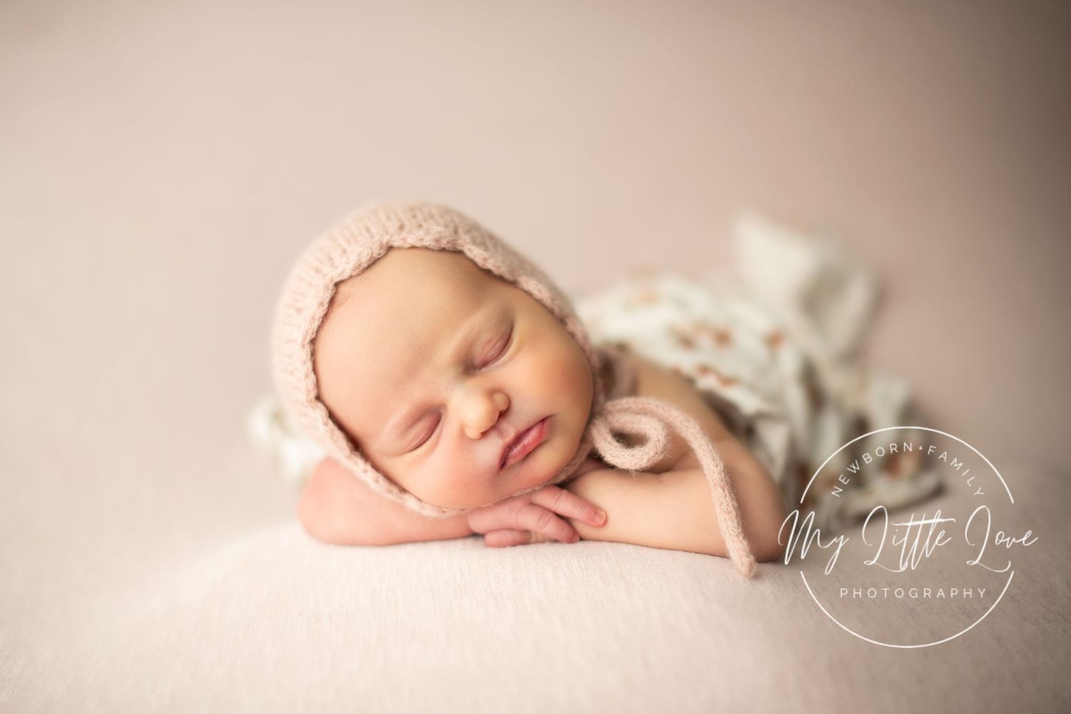 Peaceful sleeping newborn curled up on cream-colored backdrop in professional studio setting.