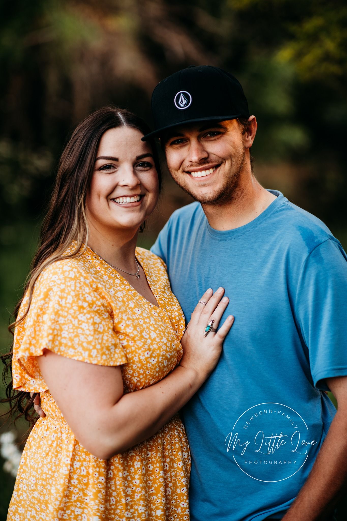 A couple in casual spring attire poses outdoors against a blurred natural background.