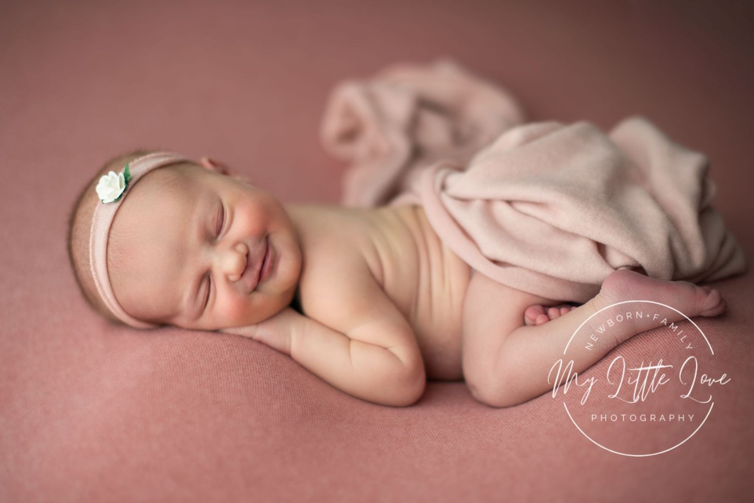 A sleeping newborn baby wrapped in soft pink blankets lies peacefully on a plush surface.