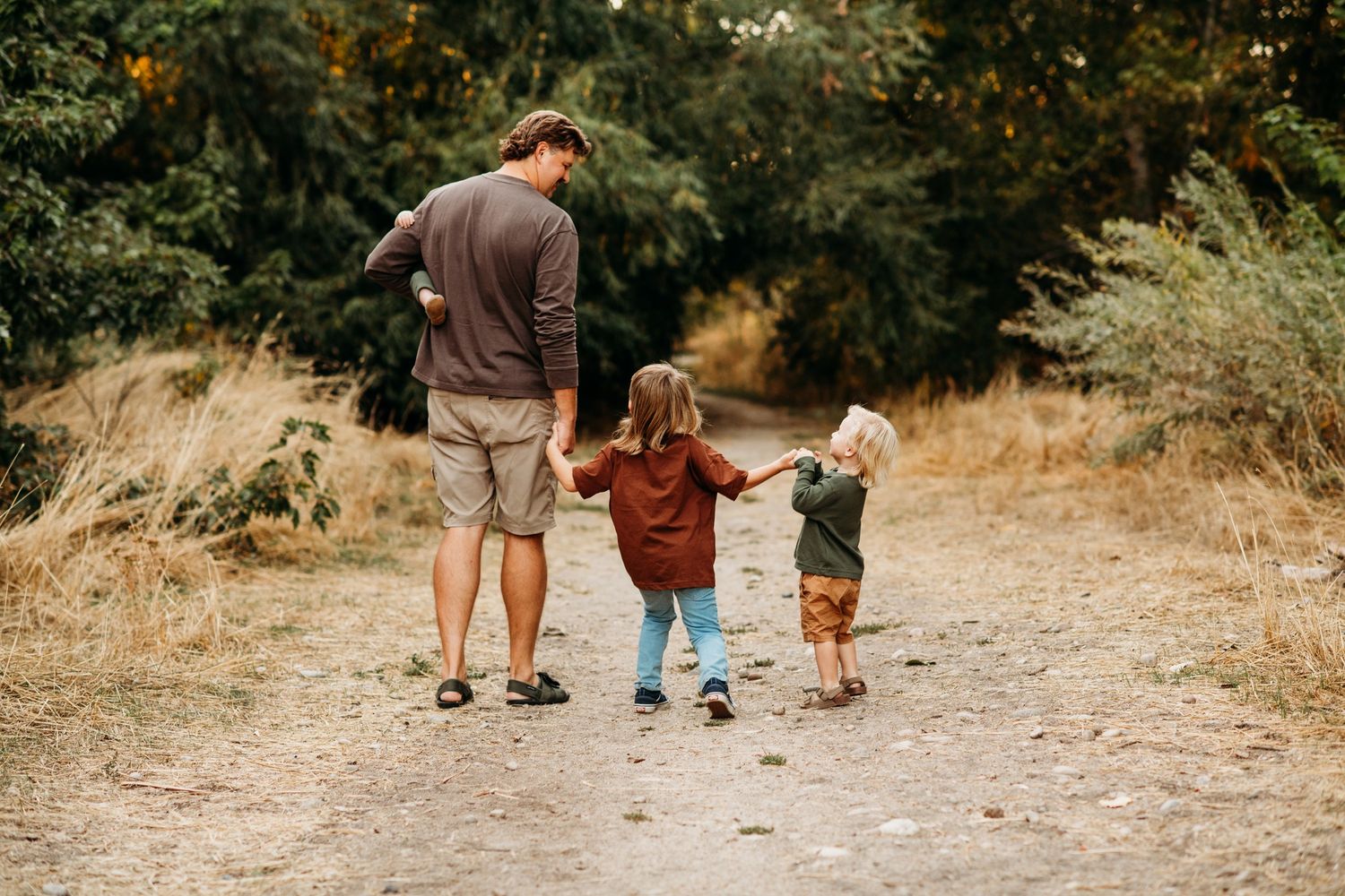 Adult and two children walk hand in hand down nature trail during summer day.