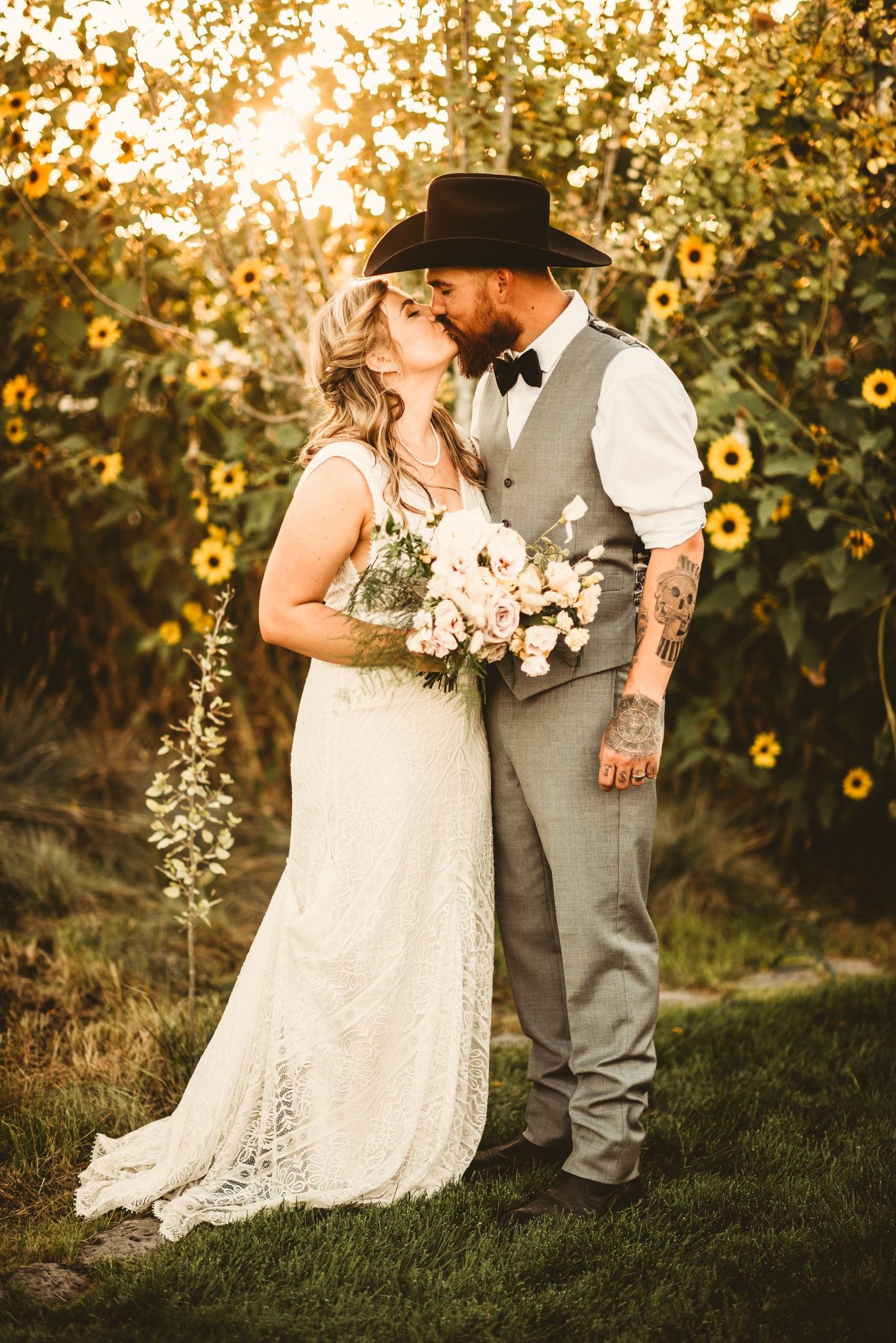 Beautiful rustic wedding couple embracing in a golden sunlit field with sunflowers and bouquet at sunset.