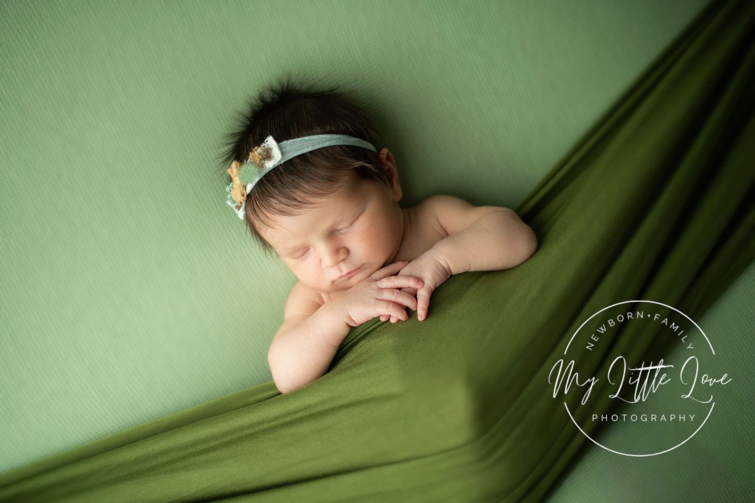 Sleeping newborn wrapped in soft green fabric against matching green backdrop in artistic portrait series.