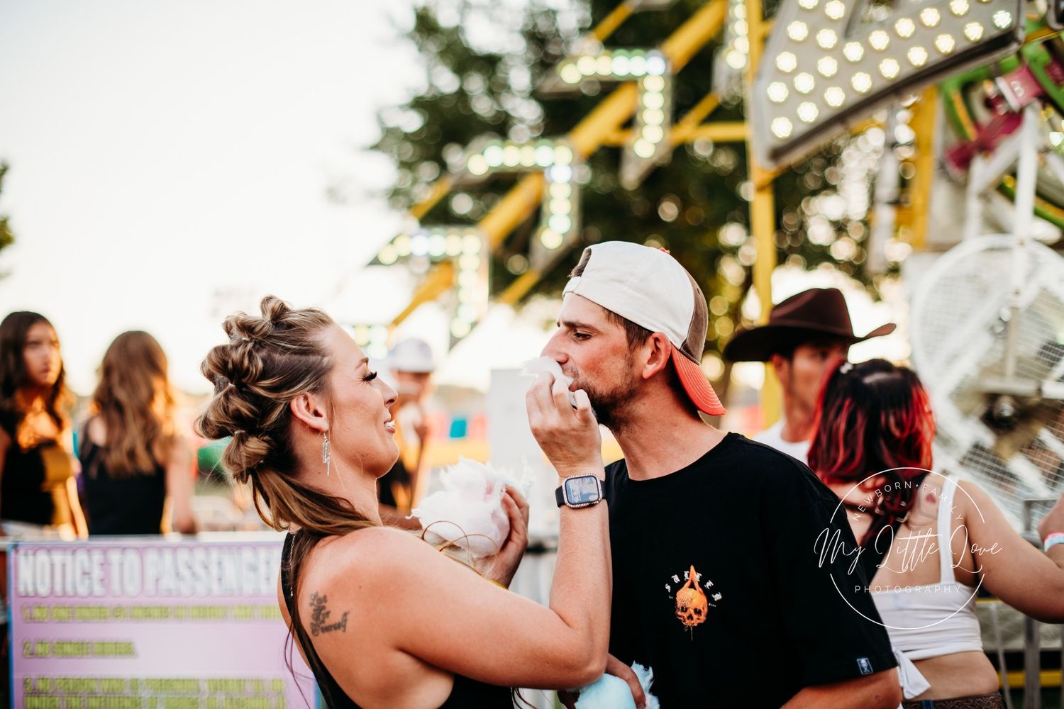 Candid moment between couple at outdoor festival with string lights in background.