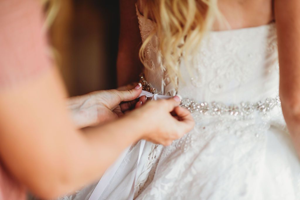 Close-up detail of adjusting a white wedding dress with delicate beaded embellishments.