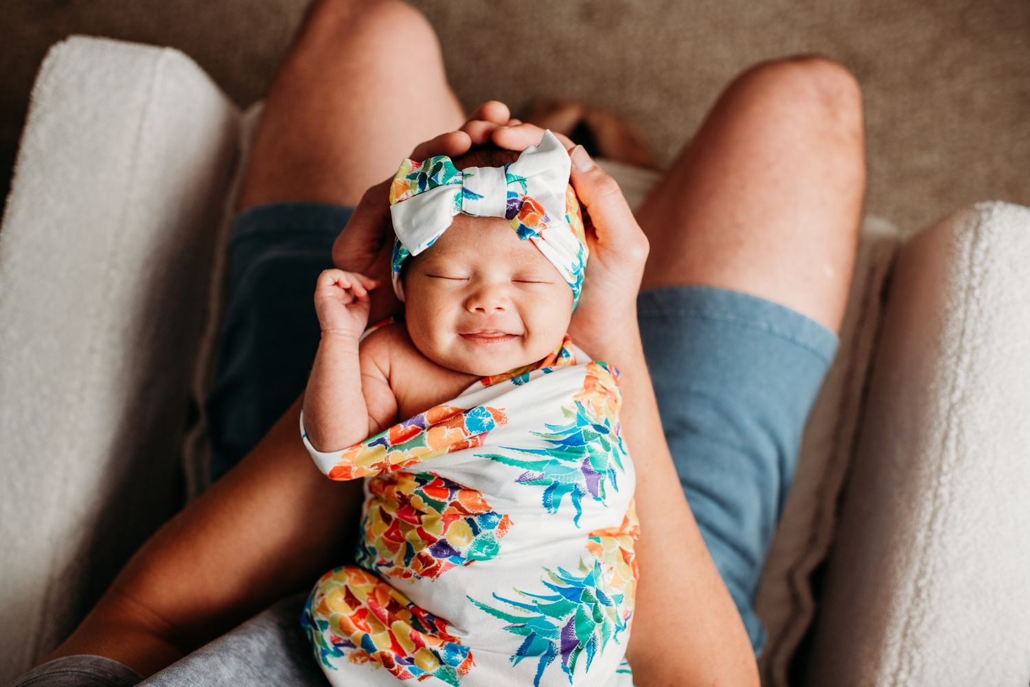 A cheerful baby wrapped in a tropical print swaddle against a light background.