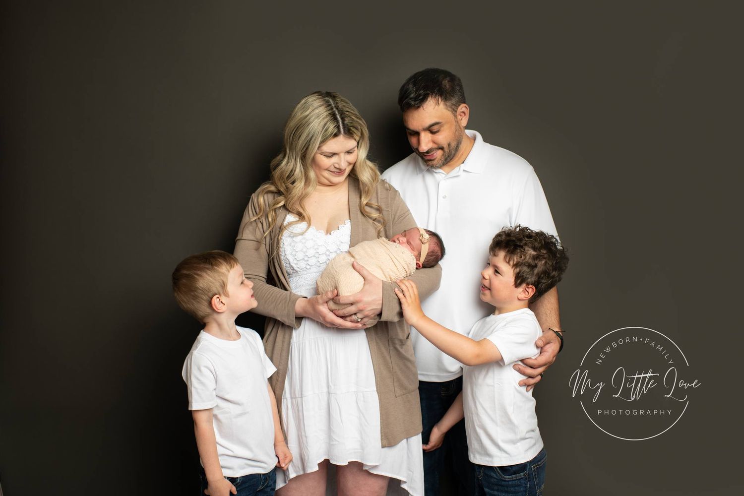 A loving family portrait in white outfits against a dark background with their new addition.