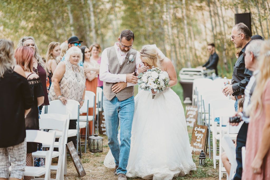 Outdoor wedding ceremony in a wooded setting with white chairs and natural decor.