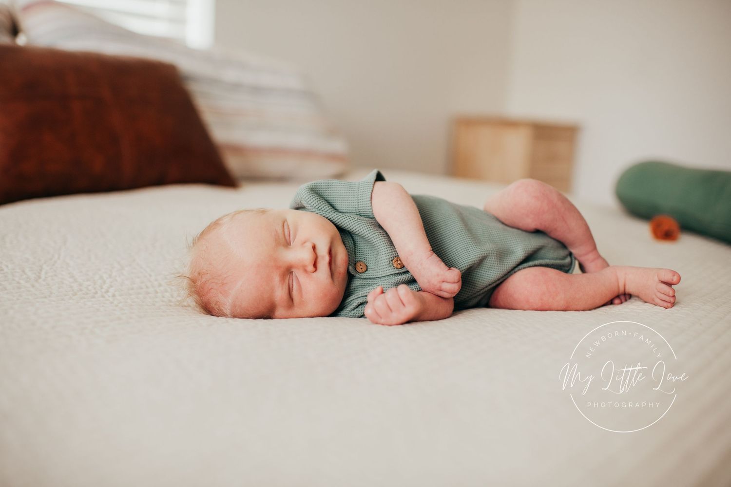A sleeping baby in mint green clothing rests peacefully on a cream-colored couch.