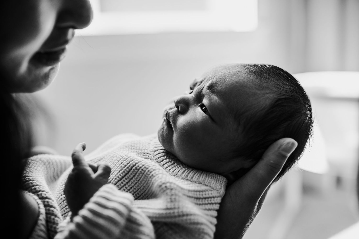 A black and white photo of a newborn baby being cradled in someone's arms while wearing a knit sweater.