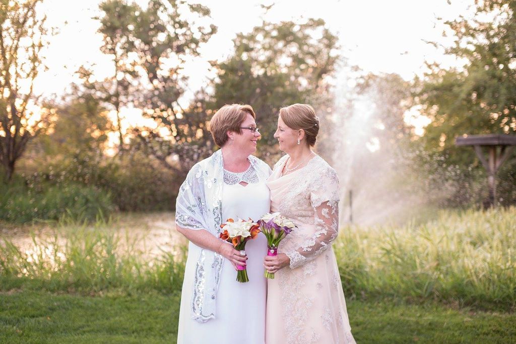 Two people in whites gowns share a romantic moment at sunset in a natural outdoor setting.