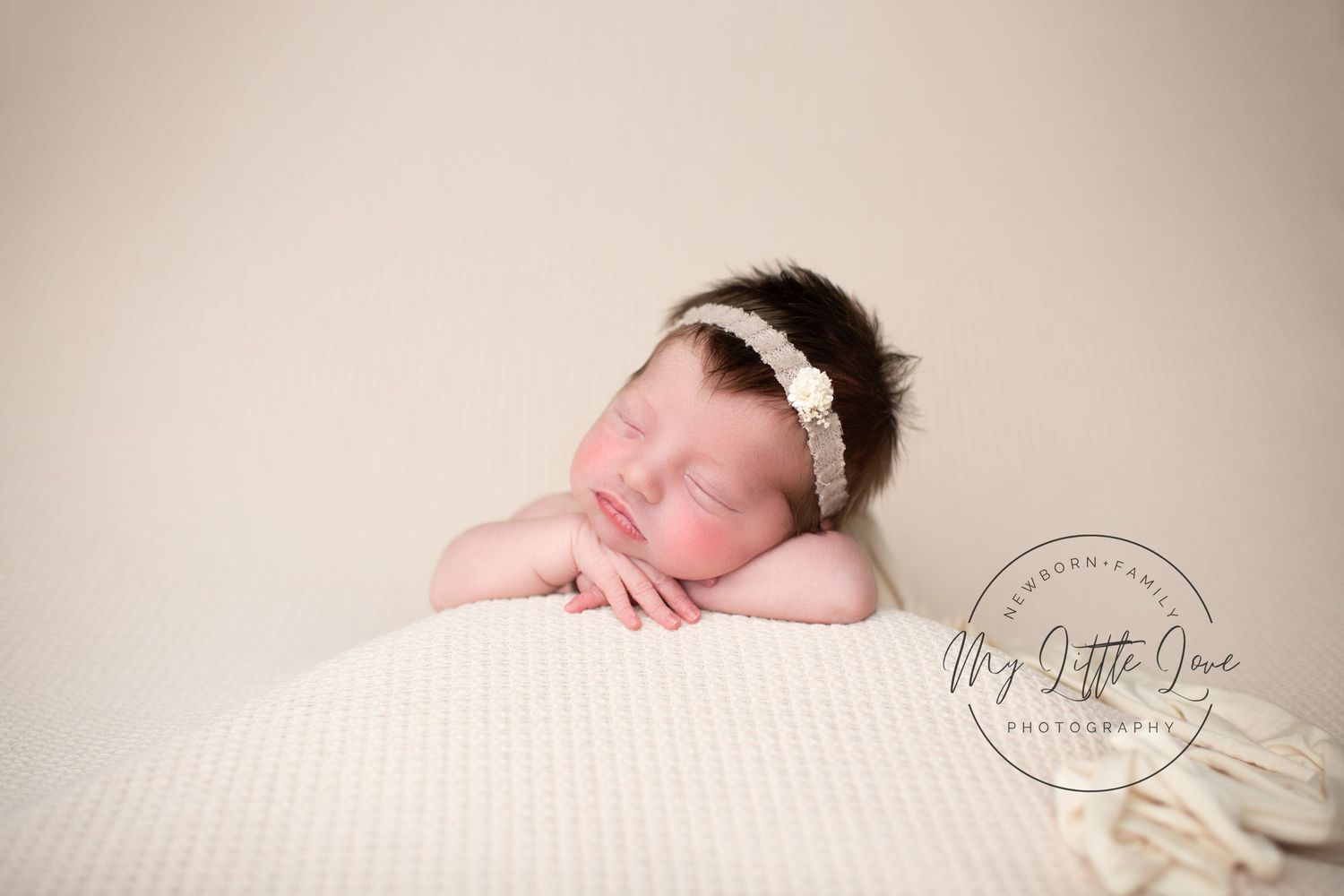 A peaceful newborn sleeping on a textured cream pillow wearing a delicate headband.