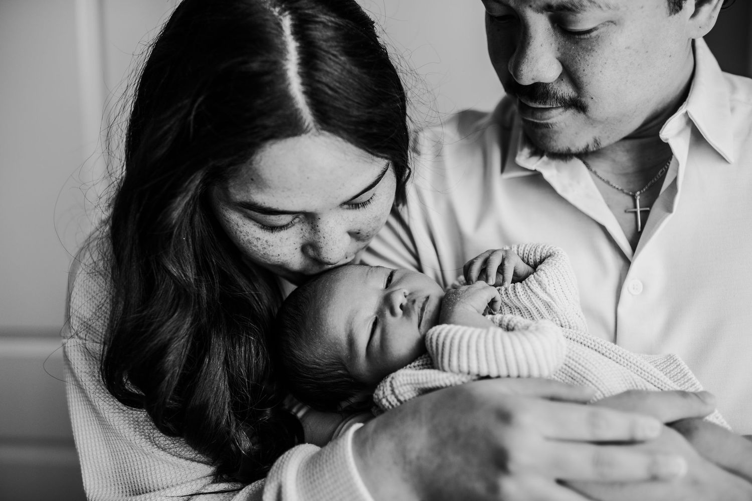 A tender black and white photo of new parents sharing an intimate moment with their newborn baby.
