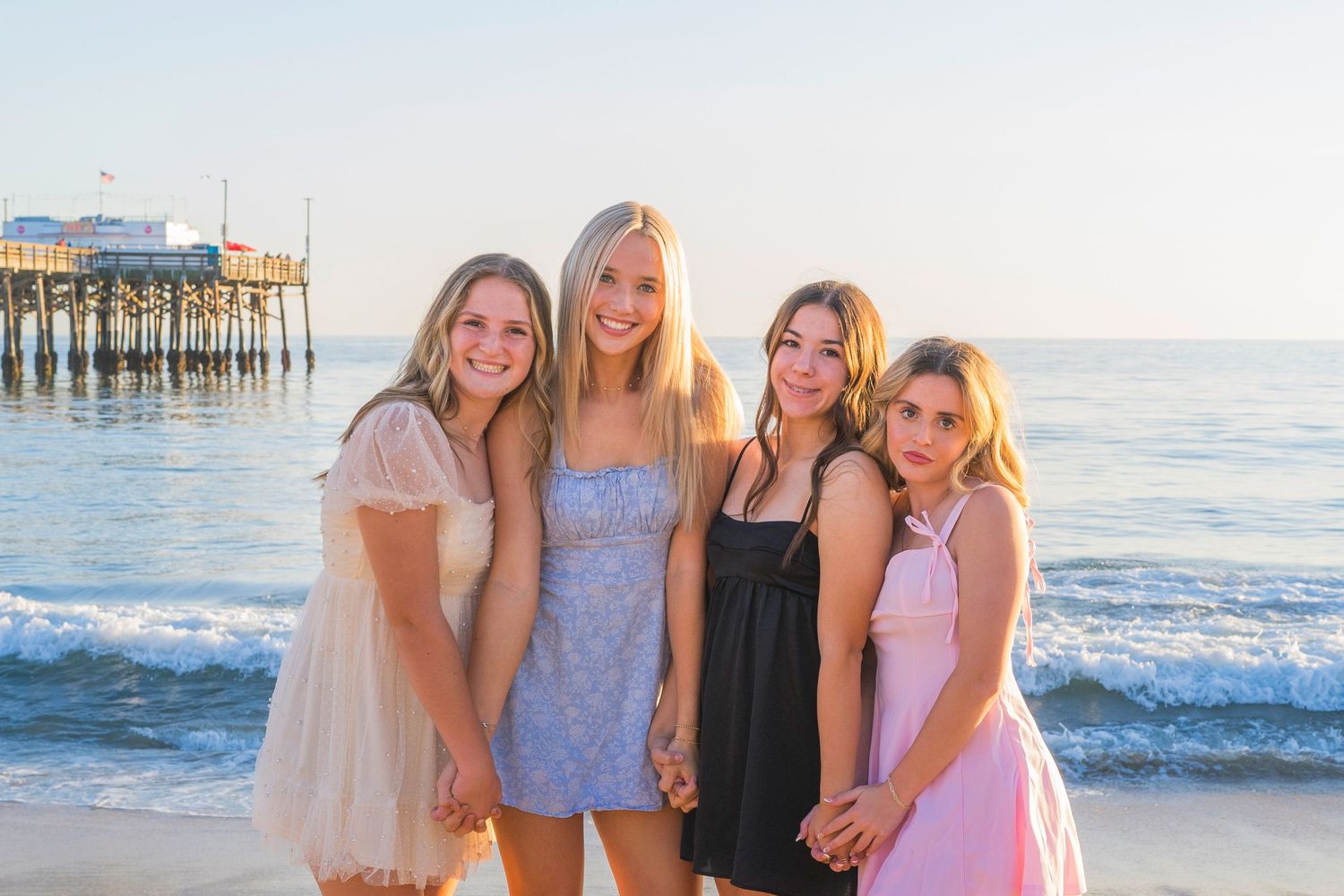 Group photo at the beach with ocean pier in background during golden hour.
