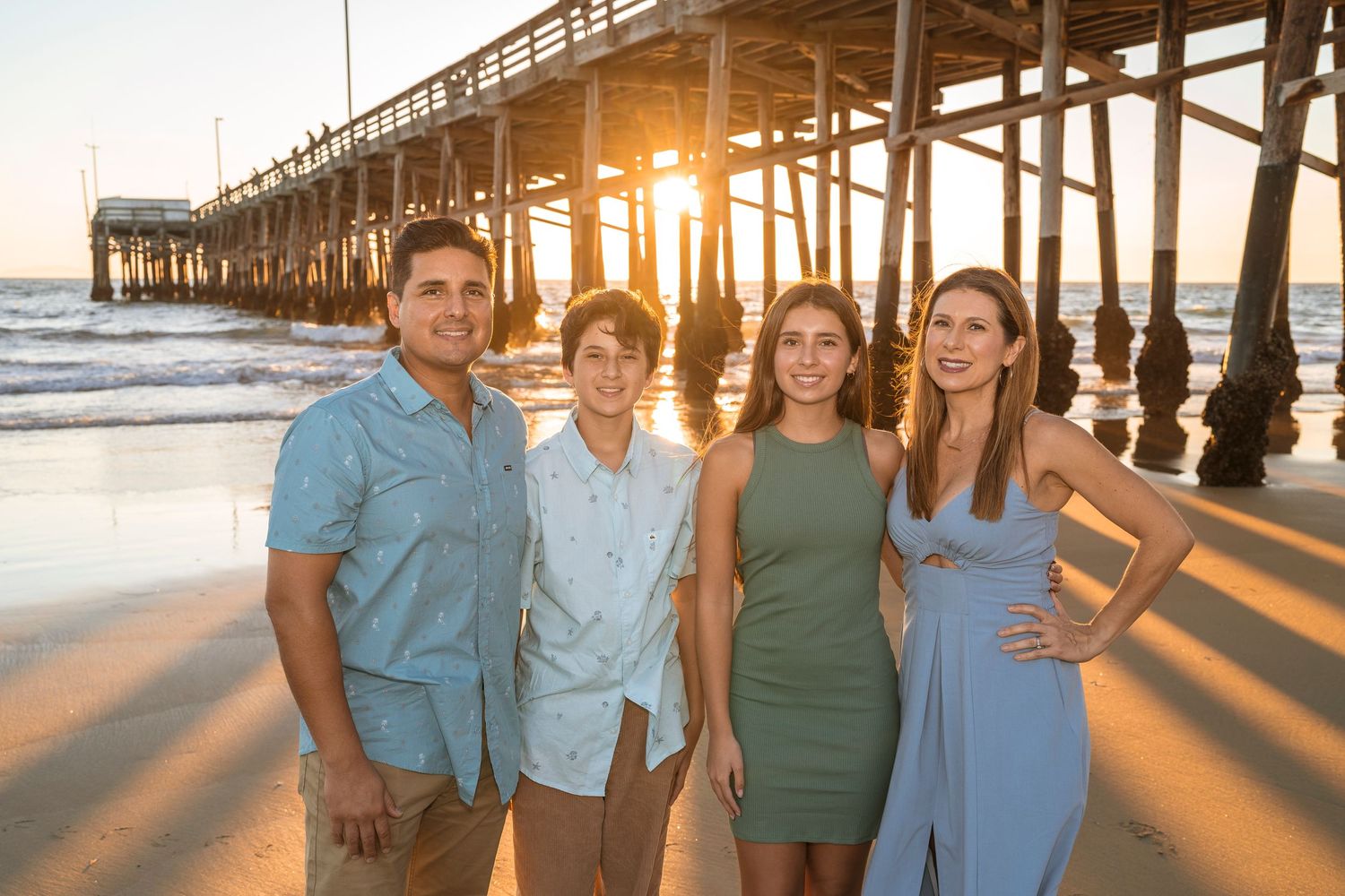 Beach family photos at sunset near a pier with long dramatic shadows.