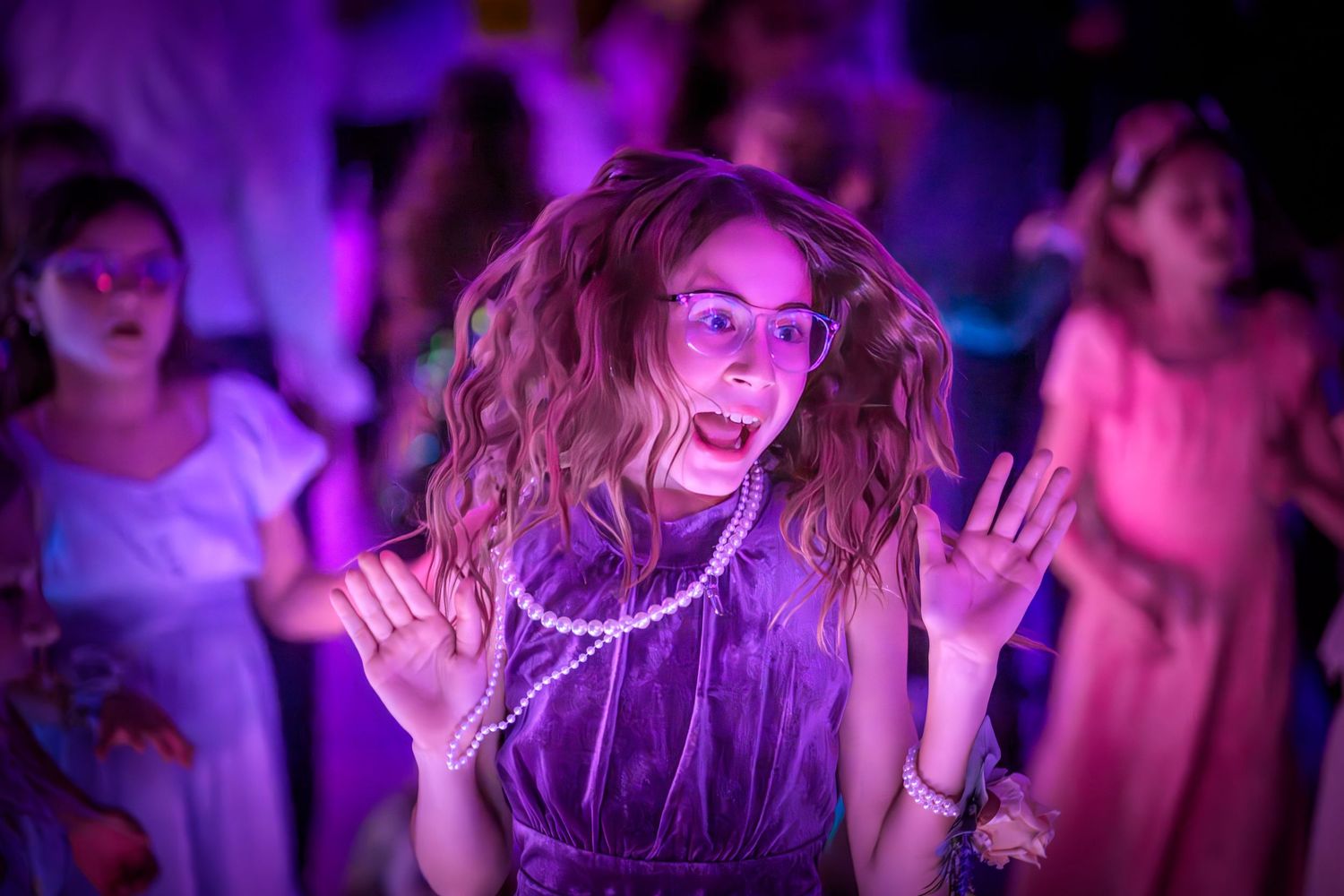 Crowd of party-goers illuminated by vibrant purple and pink lighting effects during a dance celebration.