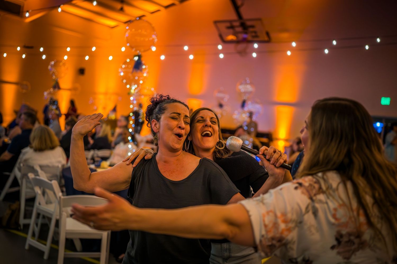Crowd enjoying entertainment in venue with orange ambient lighting and string lights overhead.