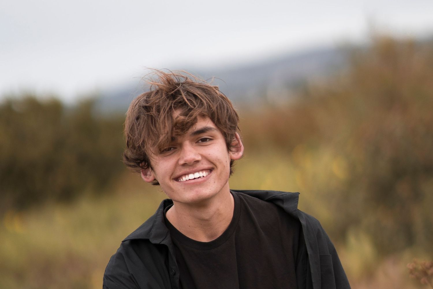 Graduate smiling outdoors with natural scenery in background.