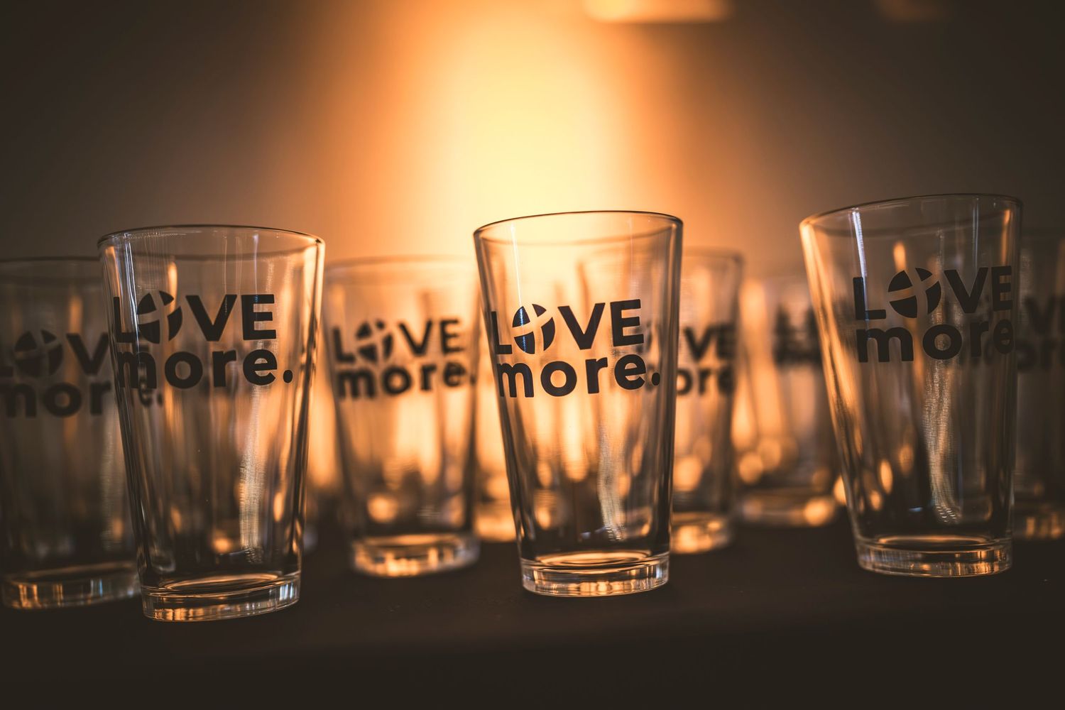 Row of glass tumblers with 'Love More' text etched on them in warm ambient lighting.