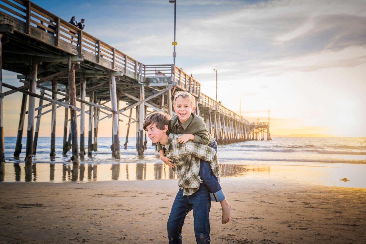 Beach photography session at a wooden pier during golden hour with waves crashing below.