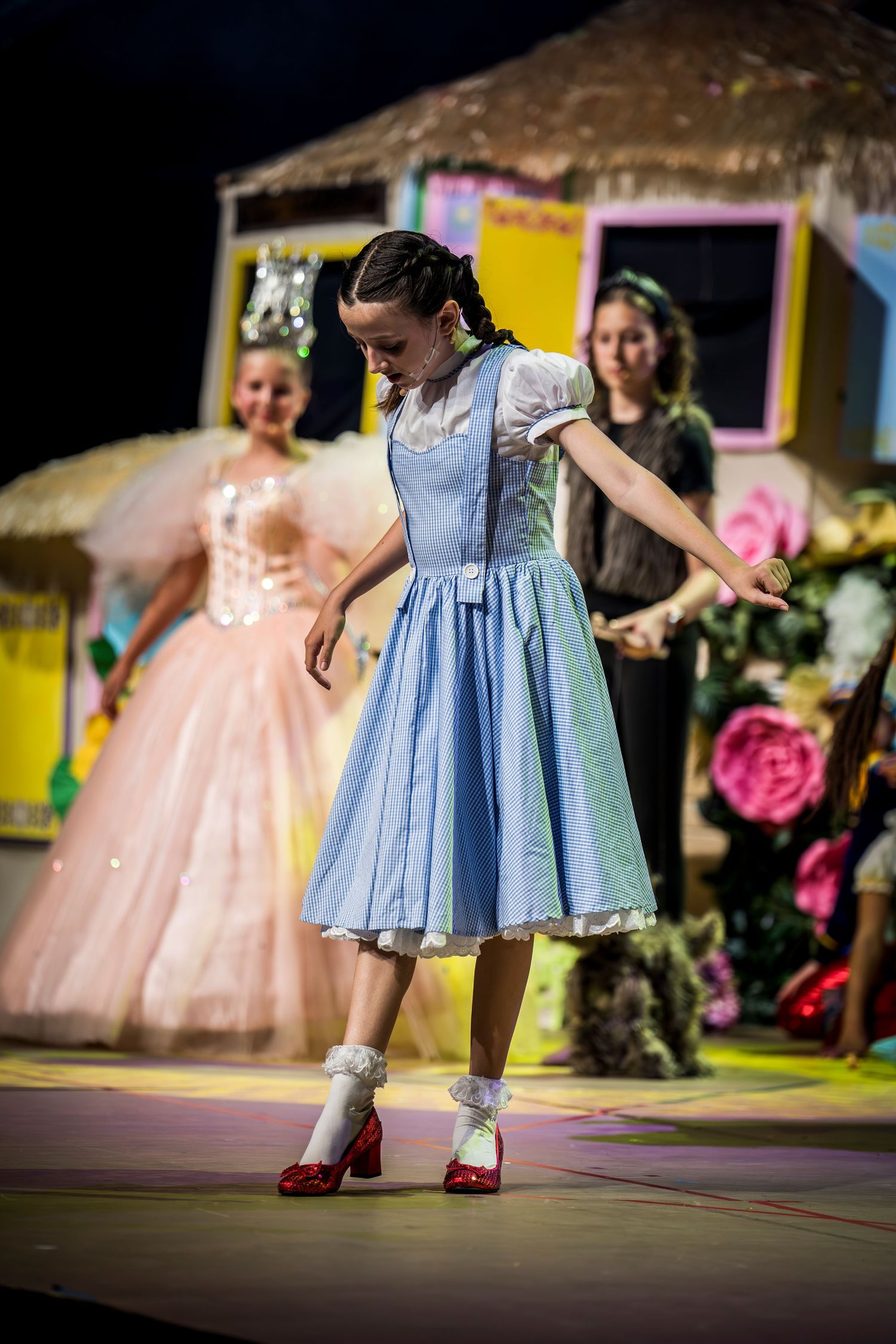Young performers in colorful dresses dancing gracefully on stage during a theatrical production.
