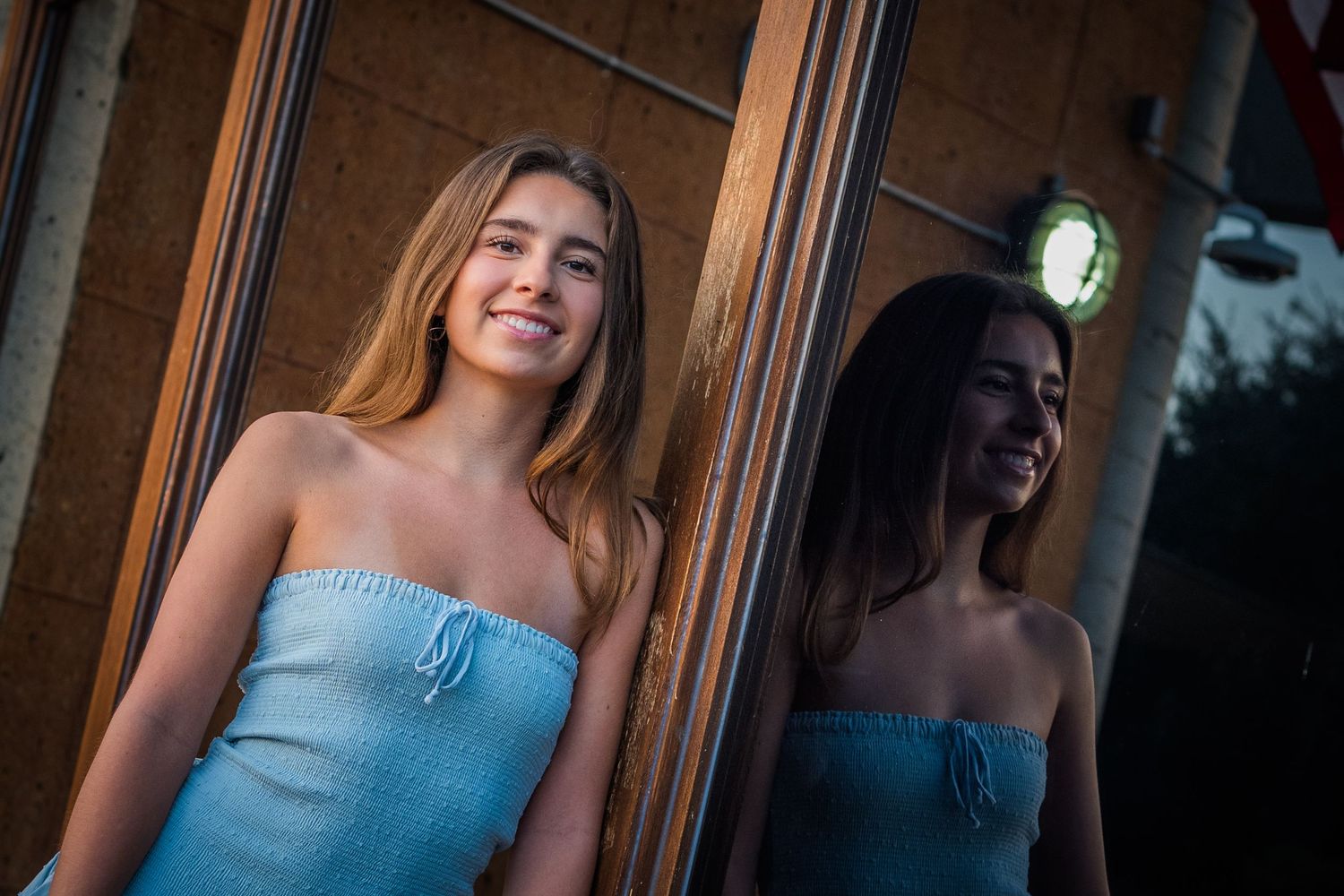 Woman in light blue dress poses against wooden door in outdoor photoshoot setting.