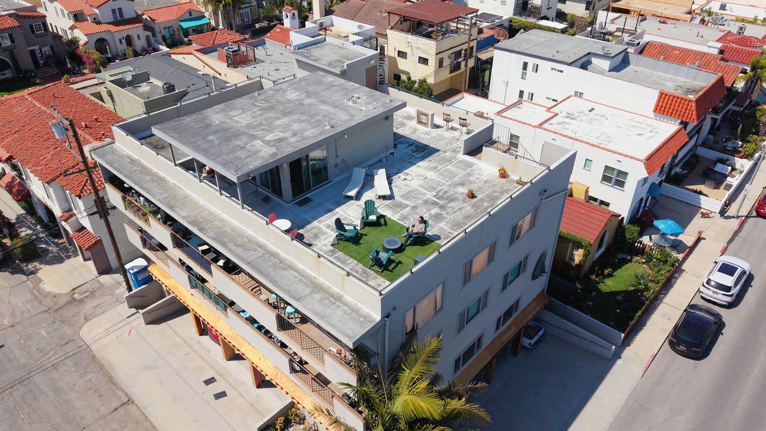 Aerial view of a modern flat-roof building with rooftop terrace and green space in a residential neighborhood.