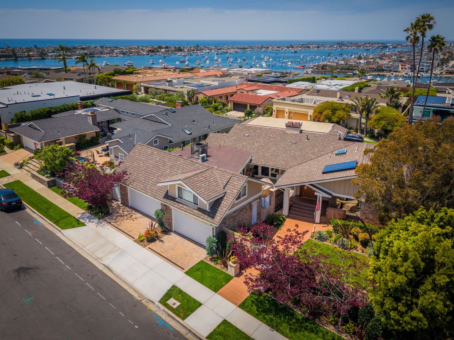 Aerial view of a coastal home with blooming trees, two-car garage, and stunning marina and ocean views in San Diego.