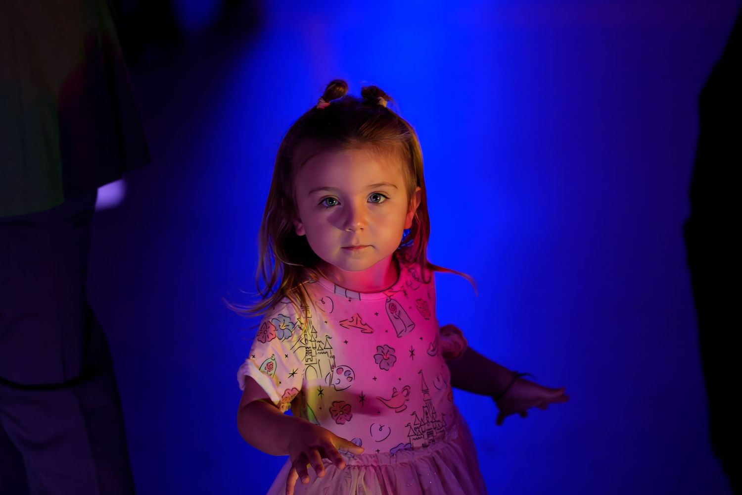 A child in a pink dress illuminated by dramatic blue and red lighting at a party.