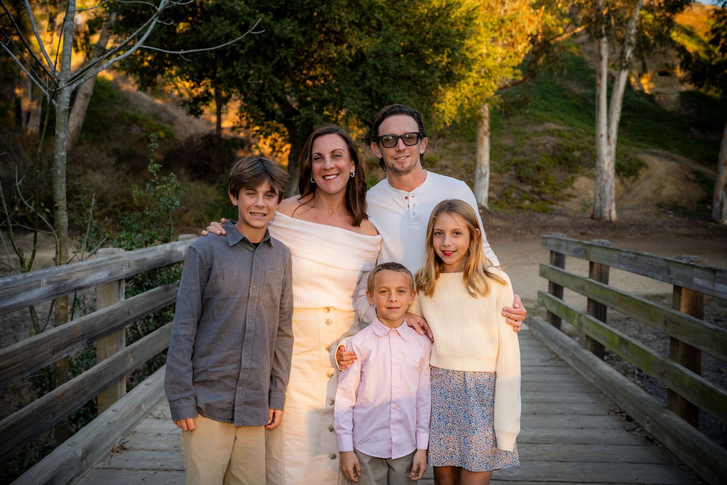 Family group portrait on a wooden bridge surrounded by autumn trees at golden hour.