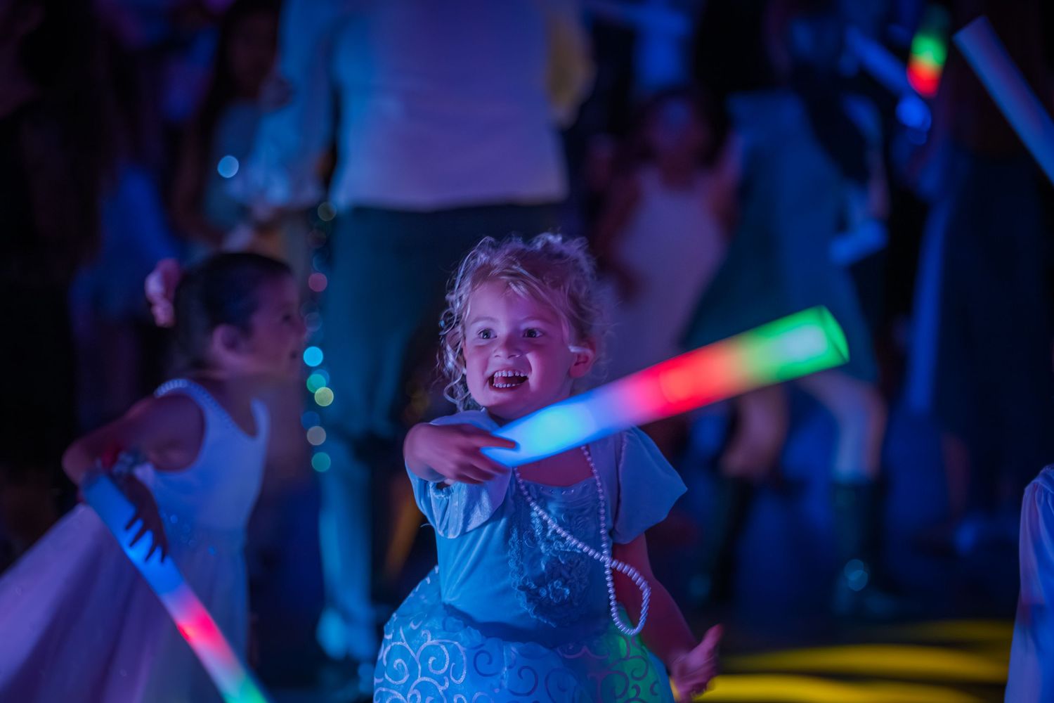 People dance and celebrate under colorful neon lights at a nighttime party event.