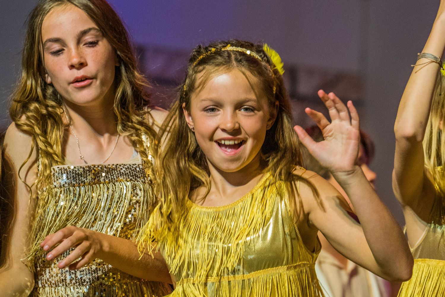 Performers in sparkly gold costumes dancing on stage under theatrical lighting.