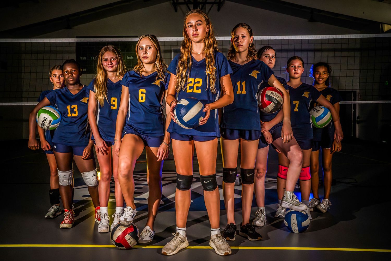 Volleyball team in blue uniforms posing together for a group photo on the court.