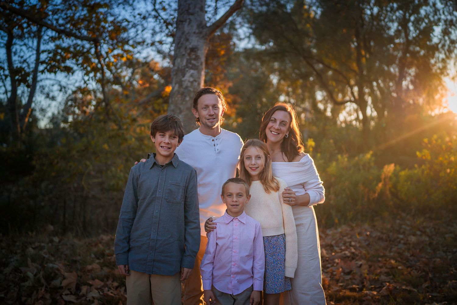 Family portrait session in a wooded area during golden hour with sun flares through the trees.