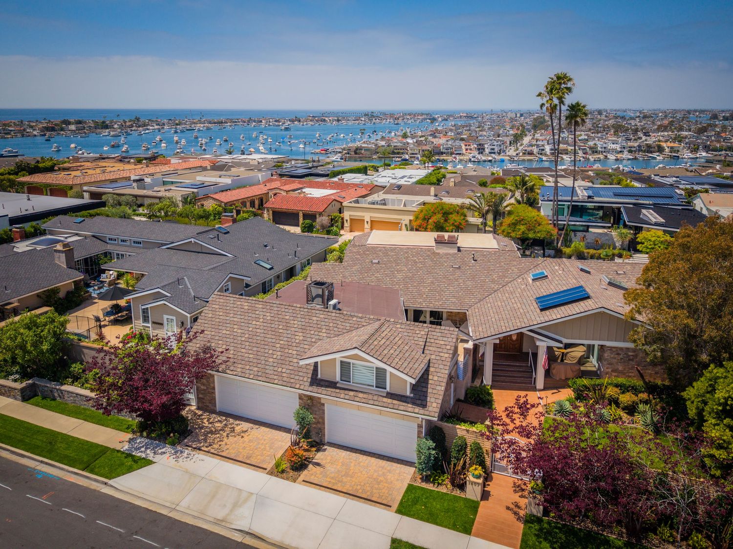 Aerial view of a coastal California home with a two-car garage, solar panels, and stunning harbor views in the background.