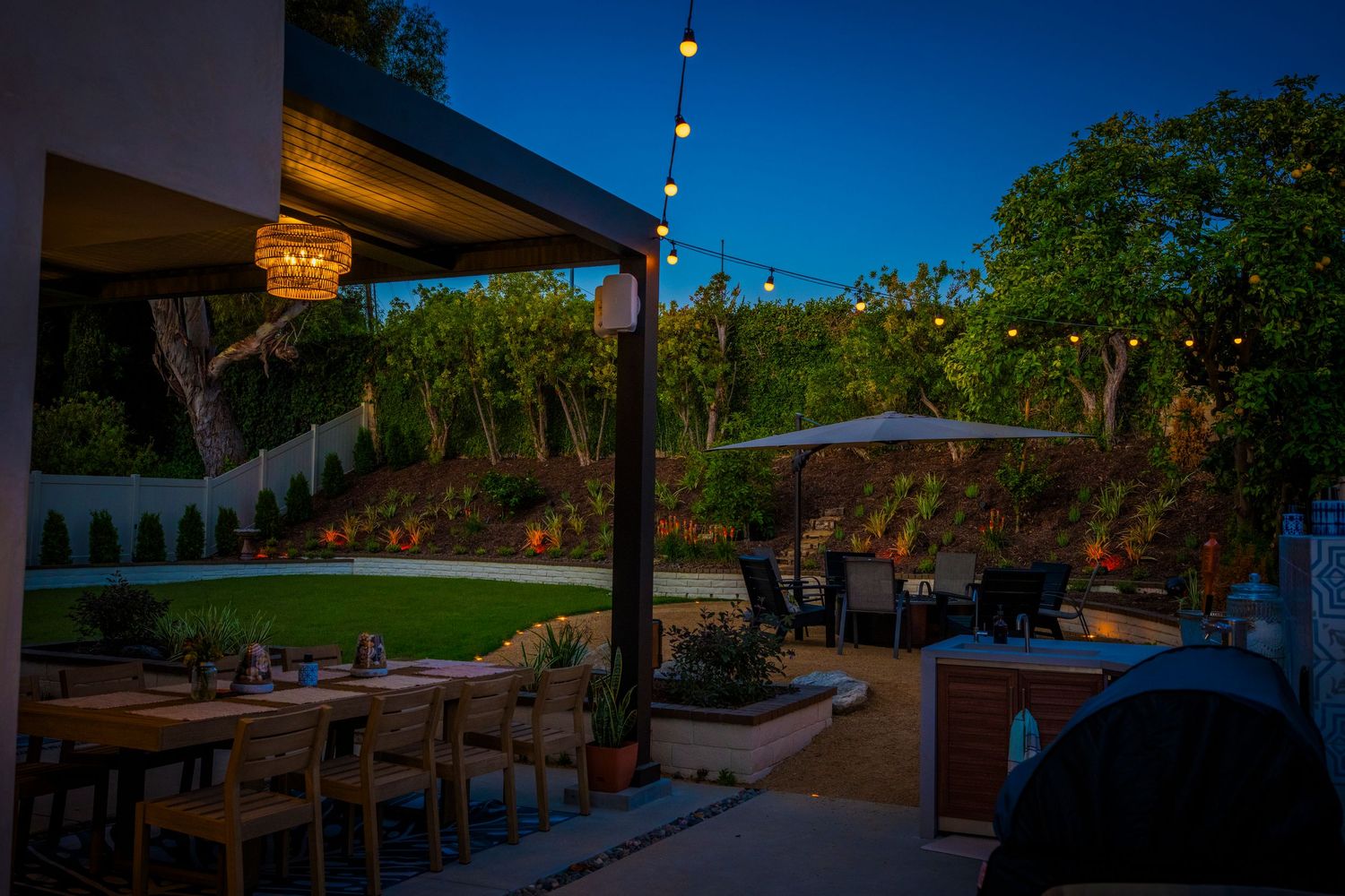 Outdoor patio panorama during blue hour showing landscaped garden and ambient lighting.