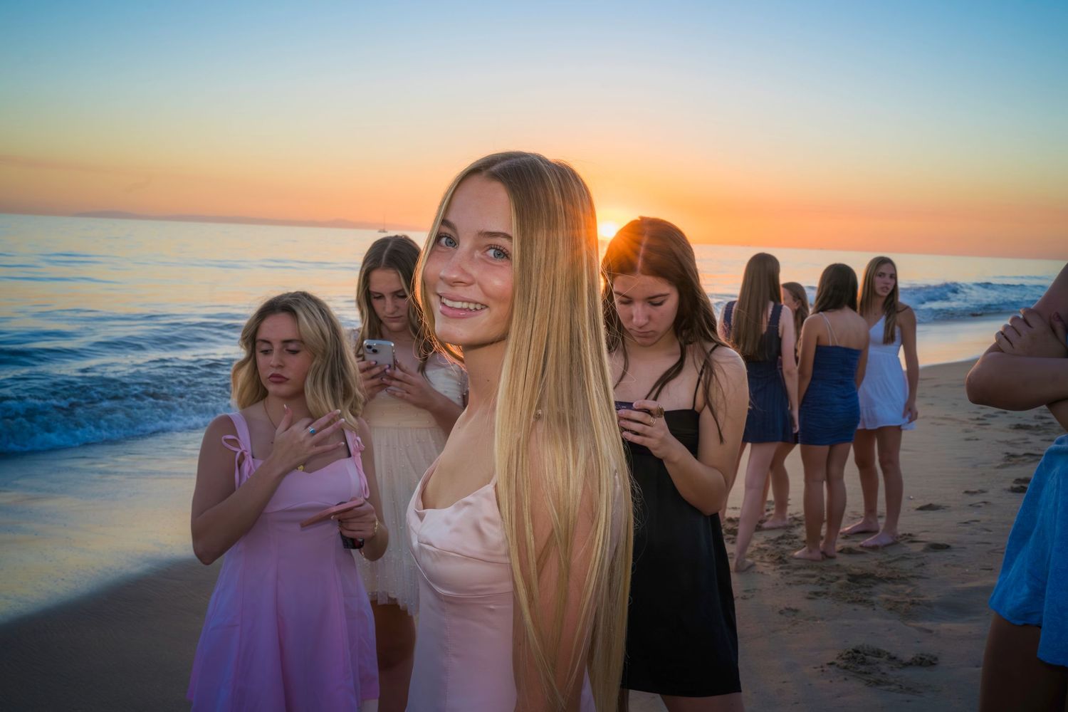 Homecoming group enjoying a beautiful beach sunset with golden light reflecting off the ocean waves.