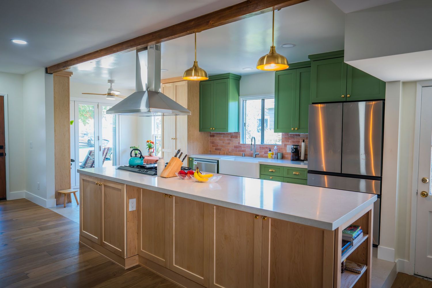 Modern kitchen with green cabinets, gold pendant lights, wood island, white countertops, and stainless steel refrigerator.