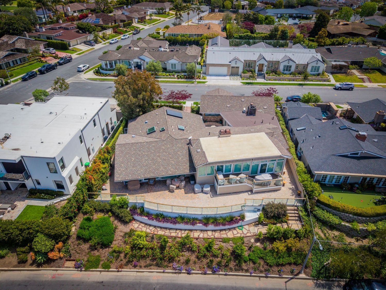 Aerial view of a large suburban home with a spacious patio, lush landscaping, and neighboring houses in a sunny residential area.